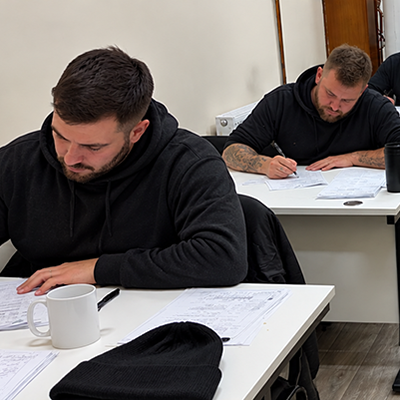 Candidates completing written exam papers in a classroom during an ACS gas reassessment course.