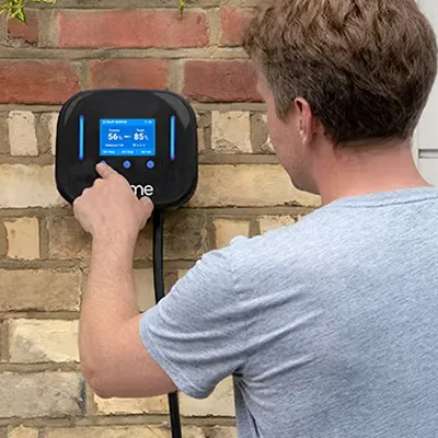 Homeowner operating a wall-mounted smart electric vehicle charger on a domestic property wall.
