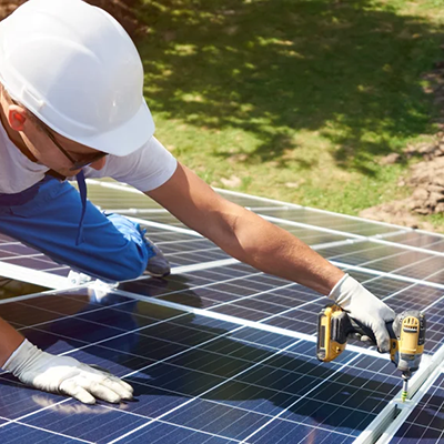 Solar installer in safety helmet using a cordless power tool to secure ground-mounted solar panels.